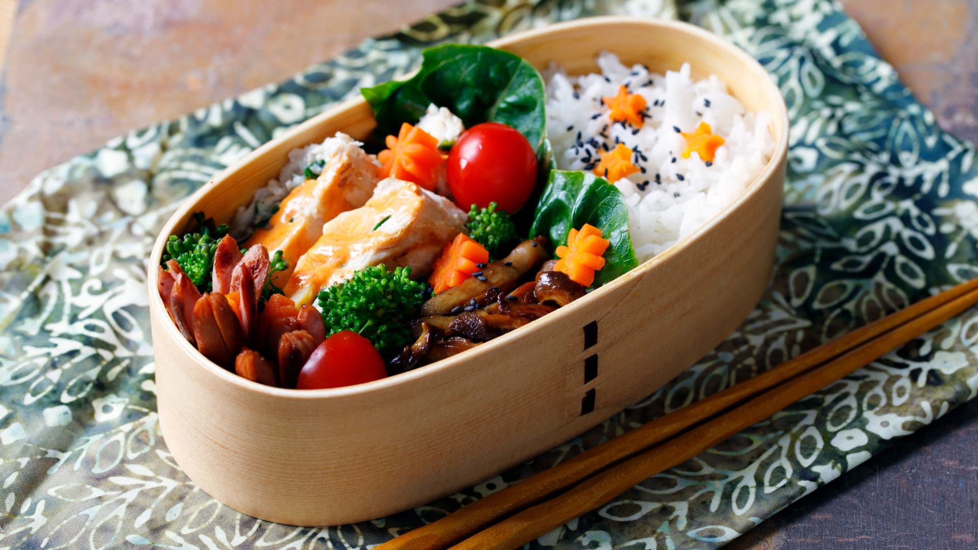 A Japanese bento box in a wooden magewappa container showing several different ingredients including chicken, vegetables, mushrooms, and rice