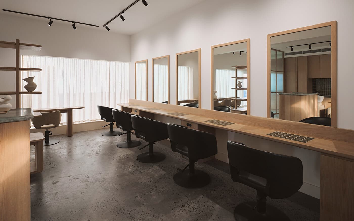 An empty modern Japanese hair salon with a row of black styling chairs, large mirrors, and a minimalist wood-and-concrete interior
