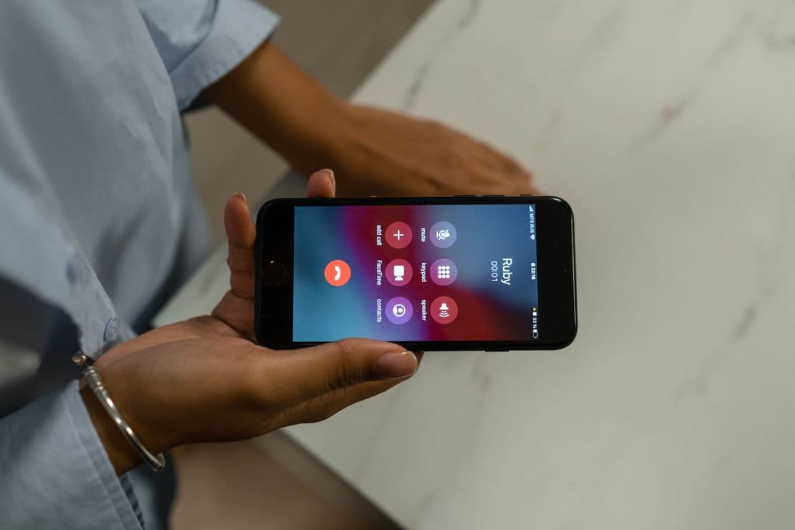 A smartphone held in two hands showing an active phone call screen with call controls